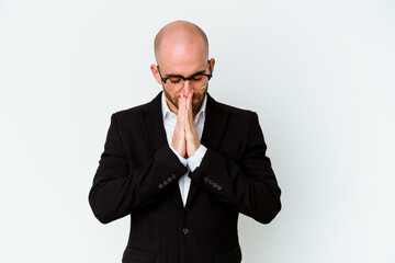 Young business caucasian bald man isolated on blue background holding hands in pray near mouth, feels confident.