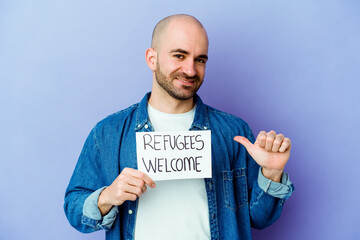 Young caucasian bald man holding a Refugees welcome placard isolated on blue background feels proud...