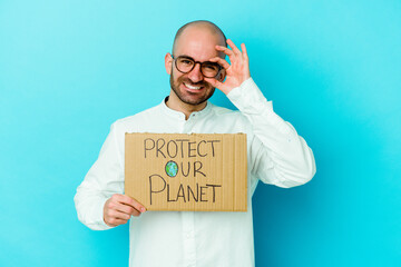 Young caucasian bald man holding a protect our planet placard isolated on purple background excited keeping ok gesture on eye.