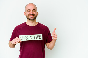 Young caucasian bald man holding a Vegan life placard isolated on purple background smiling and...