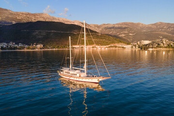 Large vintage sailboat is anchored in the middle of sea bay, illuminated by golden rays of sun....