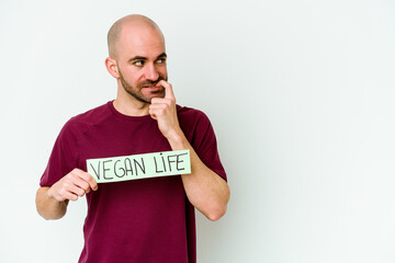 Young caucasian bald man holding a Vegan life placard isolated on purple background relaxed thinking about something looking at a copy space.