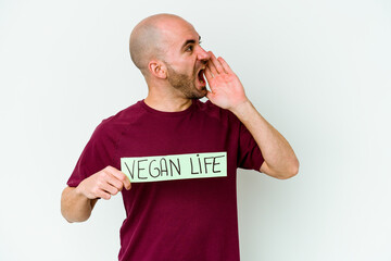 Young caucasian bald man holding a Vegan life placard isolated on purple background shouting and holding palm near opened mouth.