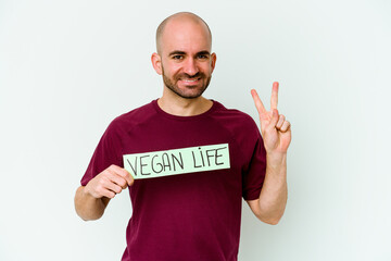 Young caucasian bald man holding a Vegan life placard isolated on purple background showing number two with fingers.