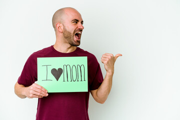 Young caucasian bald man holding a I love mom placard isolated on yellow background points with thumb finger away, laughing and carefree.