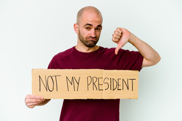 Young caucasian bald man holding a Not my president placard isolated on white background showing a...
