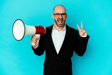 Young business bald man holding a megaphone isolated joyful and carefree showing a peace symbol with fingers.