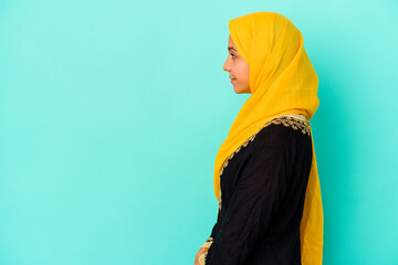 Young muslim woman isolated on blue background gazing left, sideways pose.