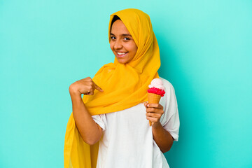 Young muslim woman eating an ice cream isolated on blue background person pointing by hand to a...