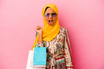 Young muslim woman shopping some clothes isolated on pink background screaming very angry and...