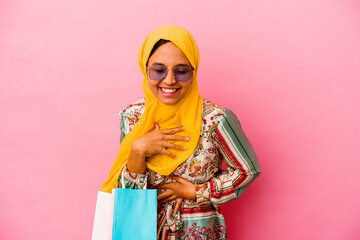 Young muslim woman shopping some clothes isolated on pink background laughing and having fun.