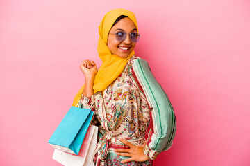 Young muslim woman shopping some clothes isolated on pink background looks aside smiling, cheerful...