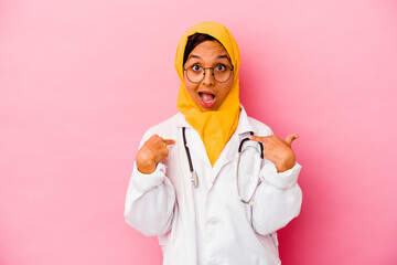 Young doctor muslim woman isolated on pink background surprised pointing with finger, smiling broadly.