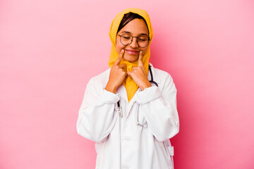 Young doctor muslim woman isolated on pink background doubting between two options.