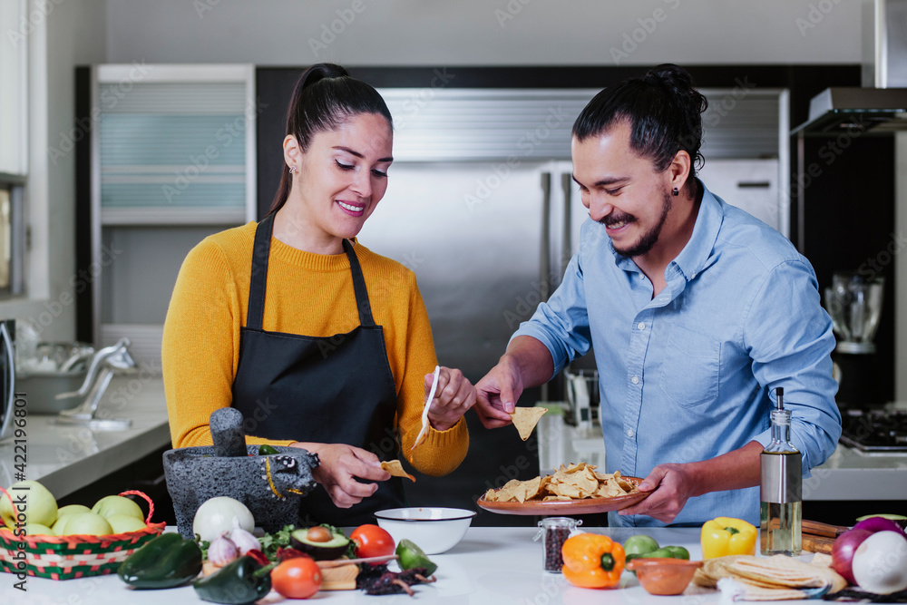 Wall mural mexican couple cooking and eating mexican food sauce together in their kitchen at home in Mexico city - Wall murals