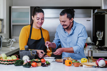 hispanic couple cooking and eating mexican food sauce together in their kitchen at home in Mexico city