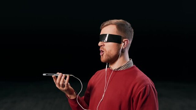 A pleasant man in headphones talks on a smartphone by voice message with glued eyes