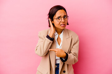Young business mixed race woman isolated on pink background trying to listening a gossip.