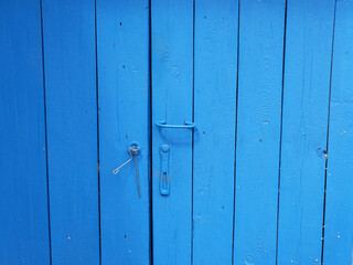 The wooden old barn door is bright blue with a metal handle. Bright