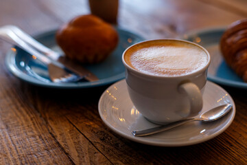 Close up hot cappuccino, latte on table with blur coffee shop background. Hot cappuccino coffee on wood table with blur croissant background. breakfast at coffee shop. softfocus select coffee