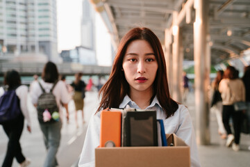 Portrait of young Asian woman holding box of items after being laid off from job due to recession and economic stress in industry