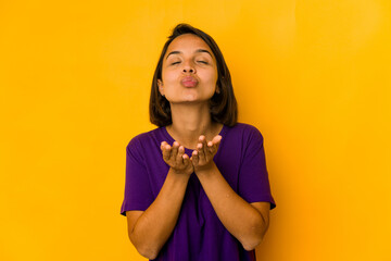 Young hispanic woman isolated on yellow folding lips and holding palms to send air kiss.