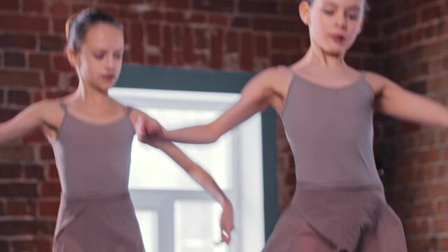 Two ballerina girls performing synchronized basic dancing in the studio
