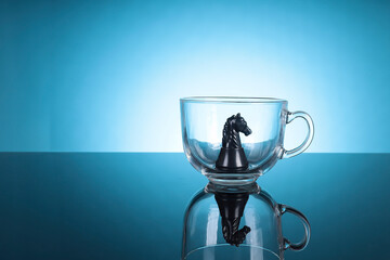 Knight chess standing inside the glass cup isolated on blue background 