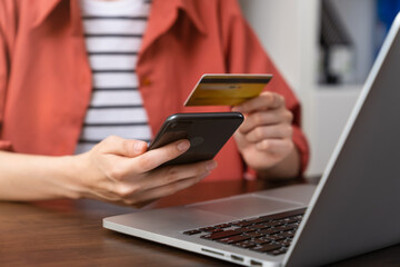 Woman hand holding a credit card and using smartphone to pay online. The concept of online shopping and payment.
