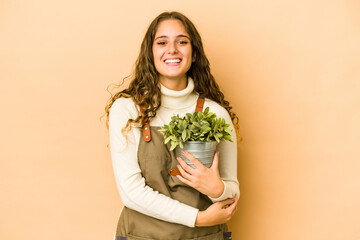 Young caucasian gardener woman holding a plant isolated laughing and having fun.