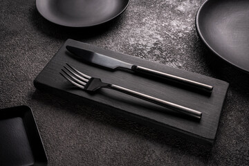 black table knife and fork surrounded by plates and dishes, close-up. The design of the restaurant,...