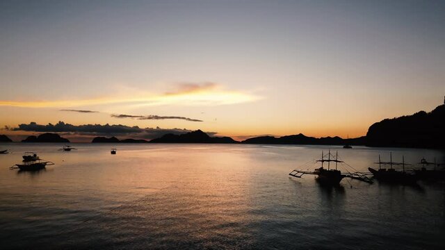 Backward low flying drone shot over water and boats at sunset in El Nido, Palawan, Philippines