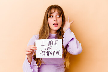 Fototapeta na wymiar Young caucasian woman holding a I hate the pandemic placard isolated trying to listening a gossip.