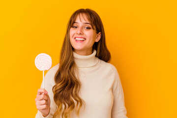 Young caucasian woman holding a lollipop isolated on yellow background happy, smiling and cheerful.
