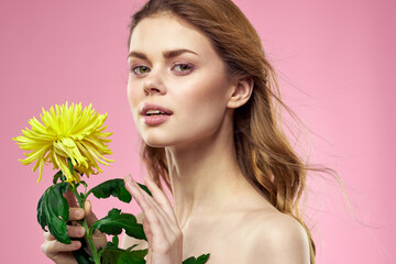 Beautiful girl with a yellow flower on a pink background nude shoulders makeup