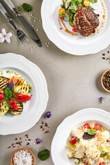 Food on luxury white plate. Beef steak, grilled vegetable and chicken caesar salad on grey textured table. Restaurant dinner gourmet menu, delicious lunch.
