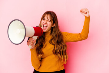 Young caucasian woman holding a megaphone isolated raising fist after a victory, winner concept.