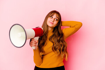 Young caucasian woman holding a megaphone isolated touching back of head, thinking and making a choice.