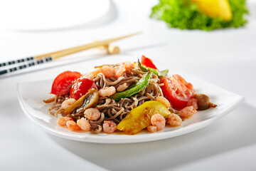 Soba noodles with seafood and vegetable. Asian style noodles food on white background. Soba in white plate with wooden choopsticks.