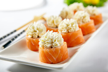 Philadelphia Sushi Roll made with Smoked Salmon. Maki sushi topped with cream cheese. White plate with wooden chopstick on white table. © Ryzhkov