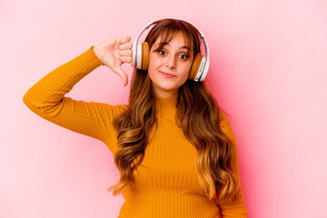 Young caucasian woman listening music with headphones isolated showing a dislike gesture, thumbs down. Disagreement concept.