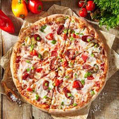 Pizza restaurant menu - Meat Pizza on parchment, topped off with meat hot sausage and pepperoni slice. Wooden table with pizza ingredients. Sunlight with harsh shadow. Rustic, natural style food.
