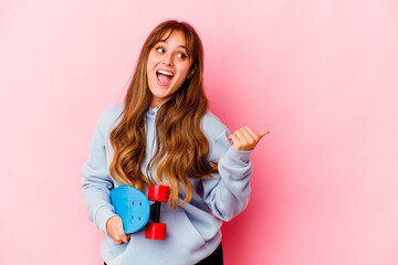 Young skater woman isolated on pink background points with thumb finger away, laughing and carefree.