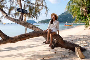 Portrait image of a beautiful young asian woman sitting on the tree by the sea