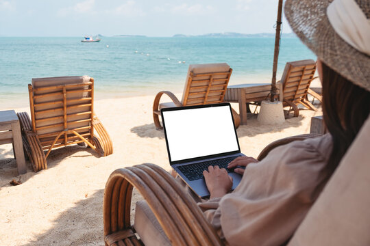 Mockup image of a woman using and typing on laptop computer with blank desktop screen while sitting on the beach
