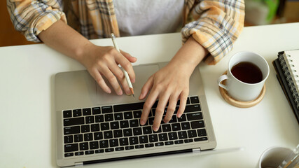Fototapeta na wymiar Female freelancer in Scott jacket hands typing on laptop keyboard on office table with coffee cup