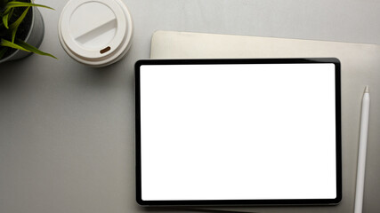 Digital tablet with mock up screen on office desk with paper cup and laptop, top view