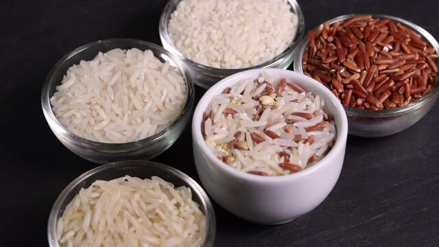 Varity mix long grain basmati medium grain jasmine short grain pilaf risotto brown low glycaemic index GI rice in glass and ceramic mini blows on black slate stone background motion drop pour spoon cl