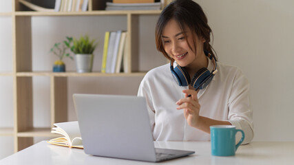 Smiling female student doing assignment with laptop and books in living room