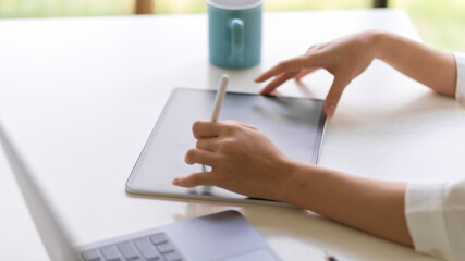 Side view of female hand with stylus pen working with digital tablet on white table